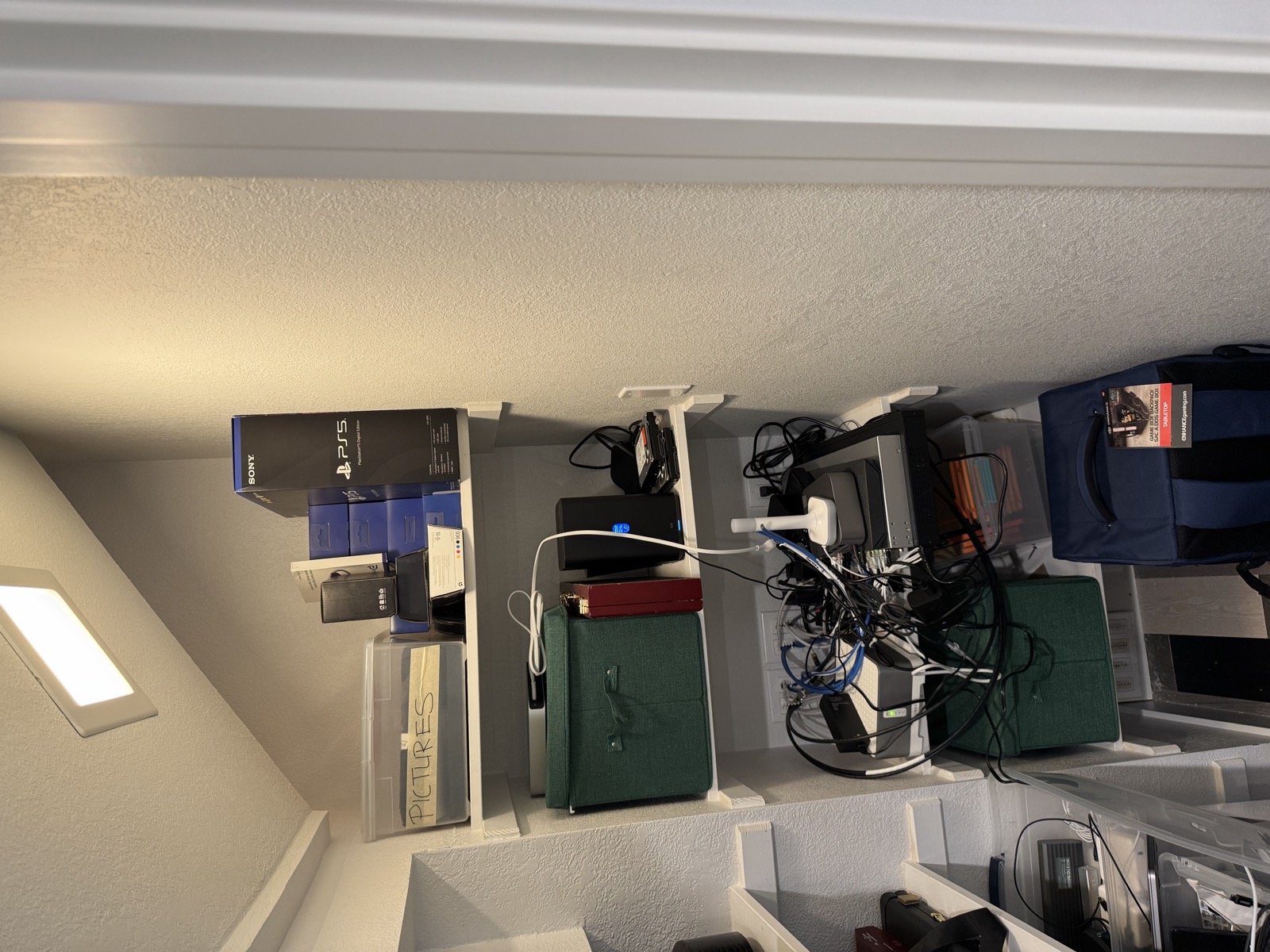 The narrow back bay: bins and boxes on the top shelves, network gear with many cables on the third shelf, wall plates behind it
